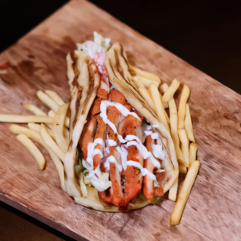 Mediterranean chicken shawarma with white sauce and french fries on a wooden board.