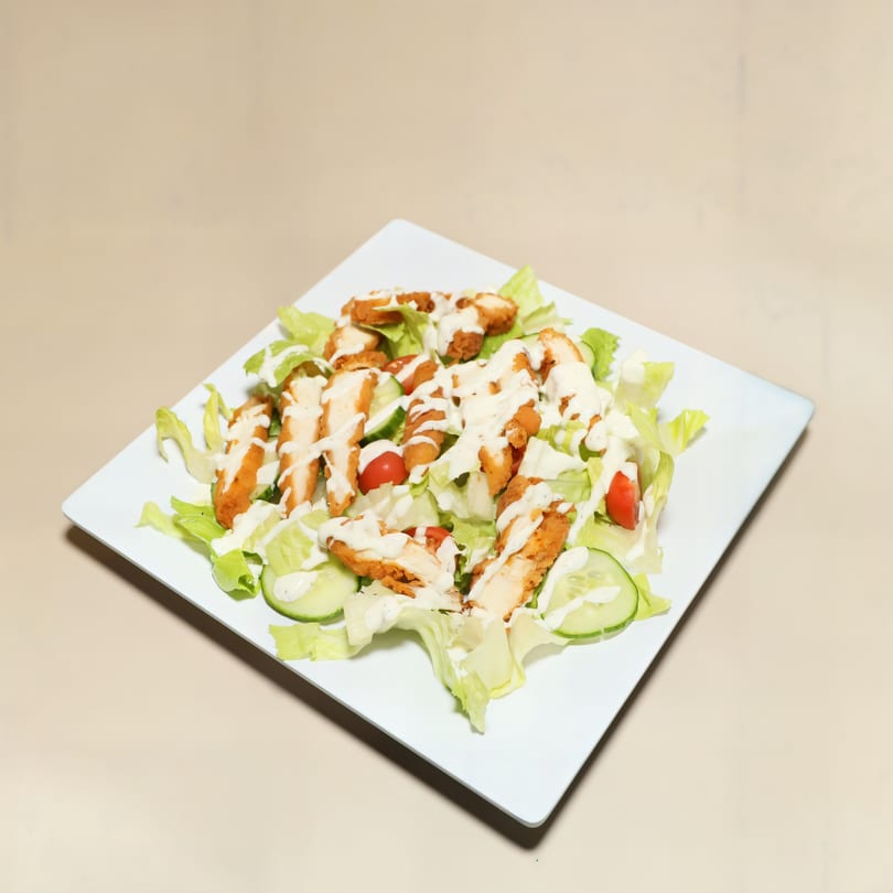 Crispy chicken salad with lettuce, cucumbers, tomatoes, and creamy dressing on a white plate.