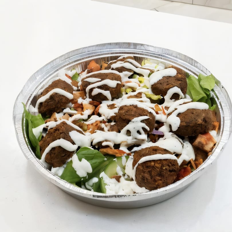 Tasty Bitez falafel bowl with white sauce, greens, and other toppings in a foil container.