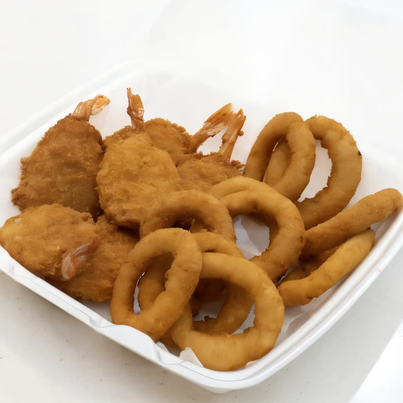 Golden-brown fried shrimp and onion rings in a white takeout container from Tasty Bitez.