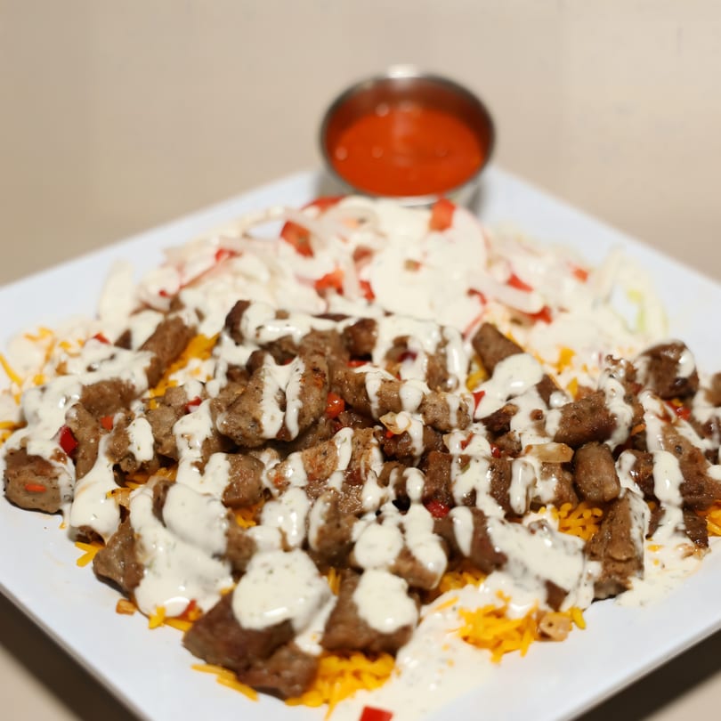 Mediterranean dish with diced meat, white sauce, shredded cheese, and a side of red sauce.